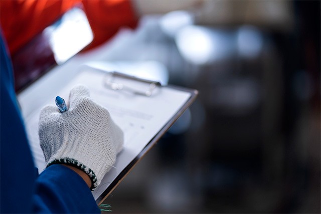 A gloved hand holding a clipboard, writing notes. The image emphasizes attention to detail and precision.